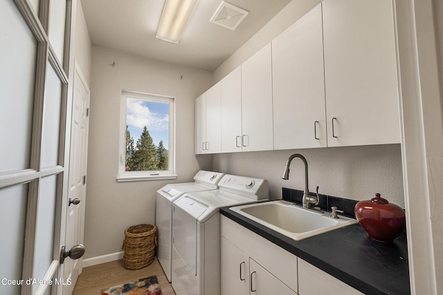clothes washing area with separate washer and dryer, a sink, light wood-style floors, visible vents, and cabinet space
