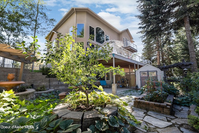 rear view of property featuring stucco siding, an outbuilding, fence, a patio, and a storage unit