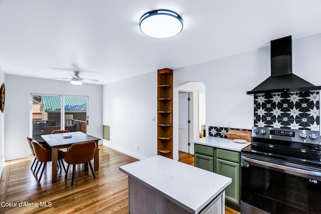 kitchen featuring ceiling fan, stainless steel electric range, wall chimney range hood, green cabinets, and hardwood / wood-style floors