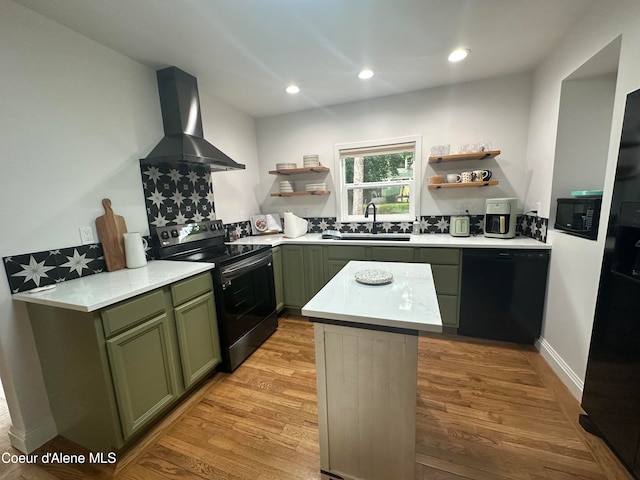 kitchen featuring light wood-type flooring, black appliances, green cabinetry, and wall chimney range hood