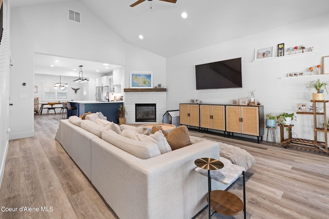 living room with high vaulted ceiling, ceiling fan, a fireplace, and light hardwood / wood-style flooring