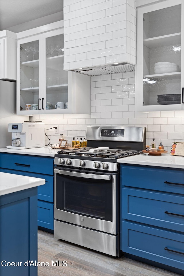 kitchen with light wood-type flooring, stainless steel gas range oven, decorative backsplash, and blue cabinetry