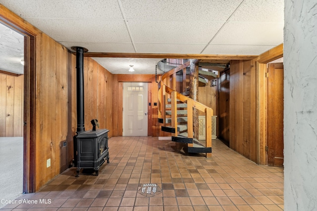 basement with a paneled ceiling, wood walls, tile patterned floors, and a wood stove