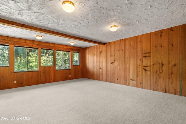 carpeted empty room featuring beamed ceiling, wood walls, and a textured ceiling