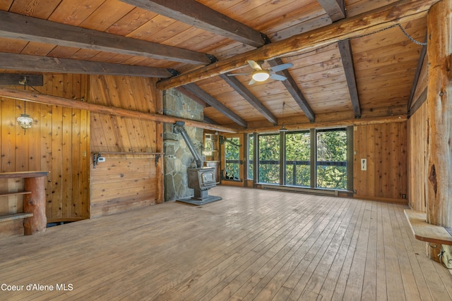 unfurnished living room featuring vaulted ceiling with beams, wood ceiling, wood walls, a wood stove, and hardwood / wood-style flooring