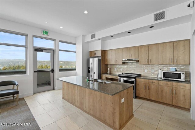 kitchen with light tile patterned floors, appliances with stainless steel finishes, a kitchen island with sink, sink, and tasteful backsplash