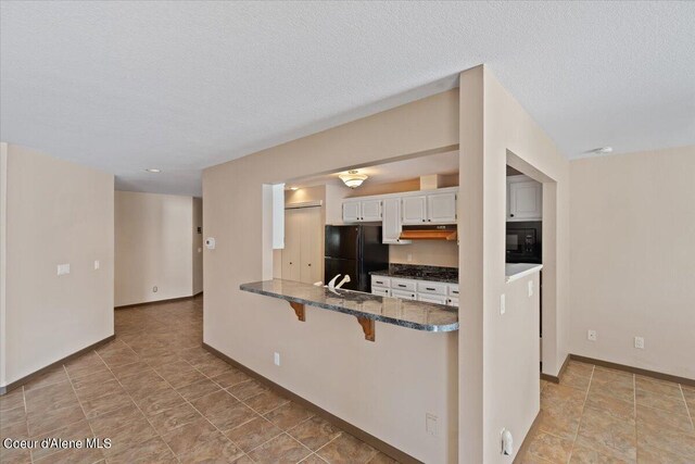 kitchen featuring white cabinets, a textured ceiling, black appliances, kitchen peninsula, and a breakfast bar