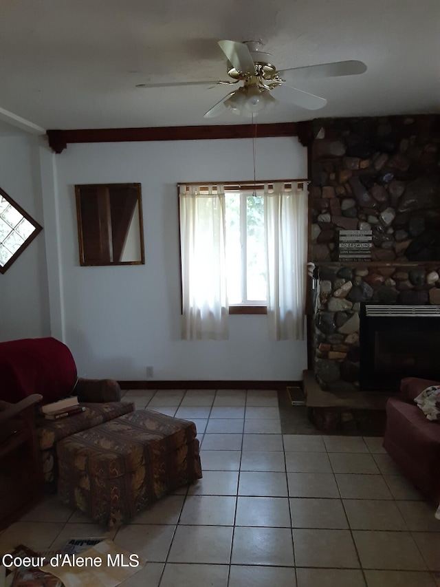 tiled living room featuring a stone fireplace and ceiling fan