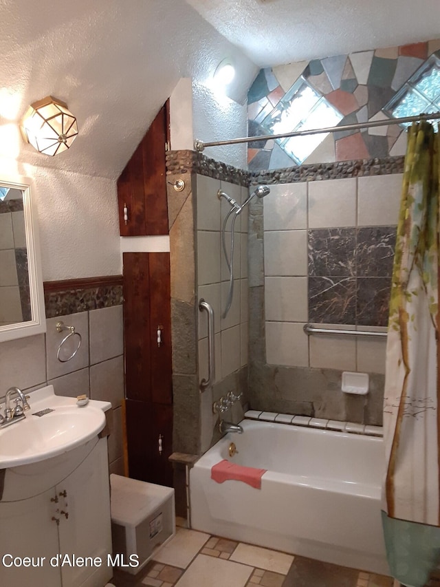 bathroom featuring shower / bath combination with curtain, tile walls, a textured ceiling, lofted ceiling, and vanity