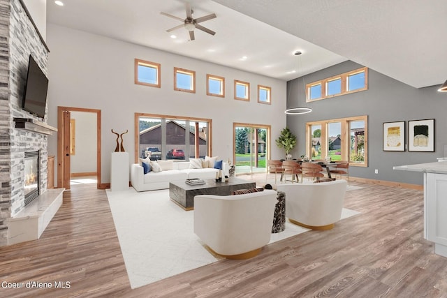 living room with a healthy amount of sunlight, a fireplace, a towering ceiling, and ceiling fan