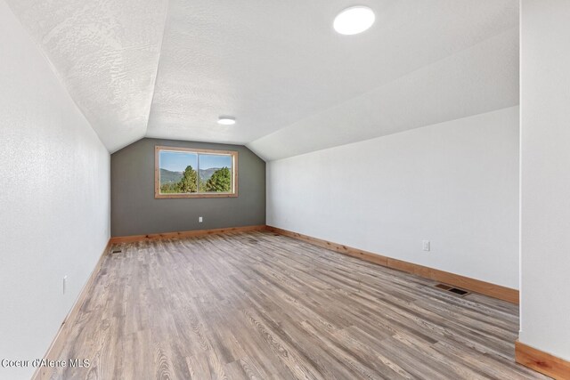 additional living space with light wood-type flooring, vaulted ceiling, and a textured ceiling