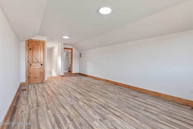 bonus room with vaulted ceiling, light hardwood / wood-style floors, and a textured ceiling