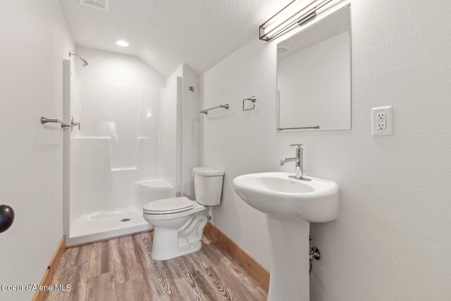 bathroom with a textured ceiling, hardwood / wood-style flooring, vaulted ceiling, walk in shower, and toilet