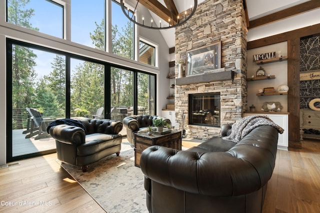 living room featuring a stone fireplace, an inviting chandelier, light hardwood / wood-style floors, and a wealth of natural light