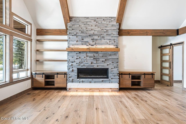 unfurnished living room with beamed ceiling, high vaulted ceiling, a barn door, a fireplace, and light hardwood / wood-style floors