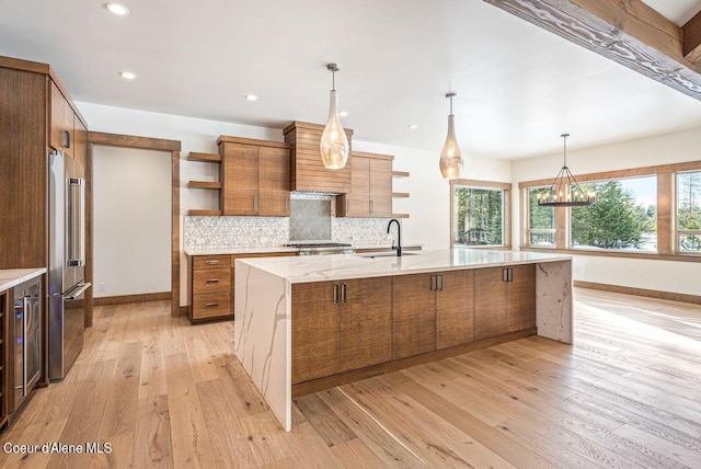 kitchen with sink, a large island, stainless steel appliances, light stone countertops, and light hardwood / wood-style floors