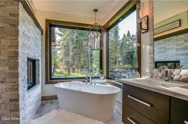 bathroom with wood-type flooring, a notable chandelier, a tub, a stone fireplace, and vanity