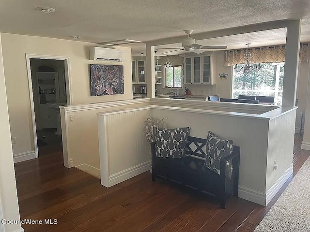 kitchen featuring pendant lighting, a textured ceiling, dark wood-type flooring, ceiling fan with notable chandelier, and a wall mounted air conditioner