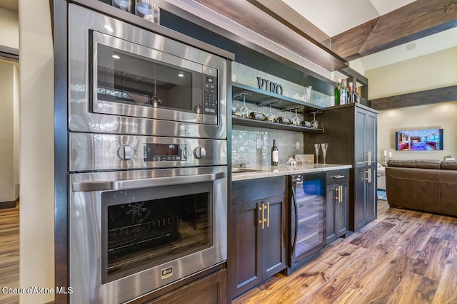 bar with light stone counters, beverage cooler, light hardwood / wood-style flooring, stainless steel appliances, and backsplash