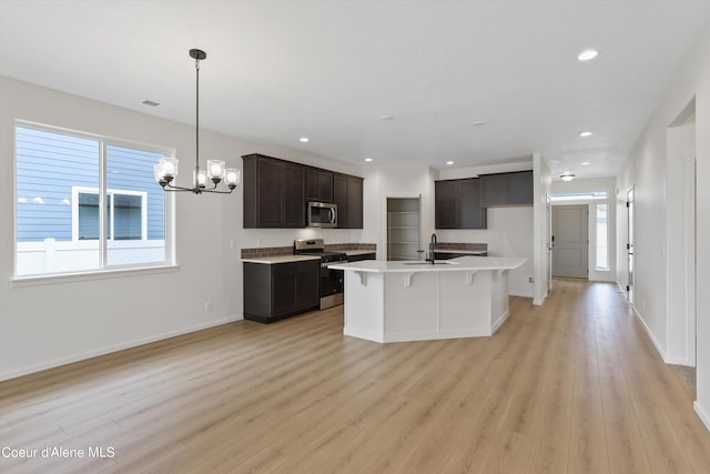 kitchen with hanging light fixtures, stainless steel appliances, light wood-type flooring, an inviting chandelier, and a center island with sink