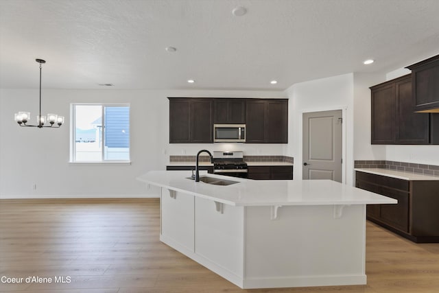 kitchen with sink, a center island with sink, appliances with stainless steel finishes, an inviting chandelier, and light hardwood / wood-style floors