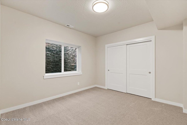 unfurnished bedroom with light colored carpet, a textured ceiling, and a closet