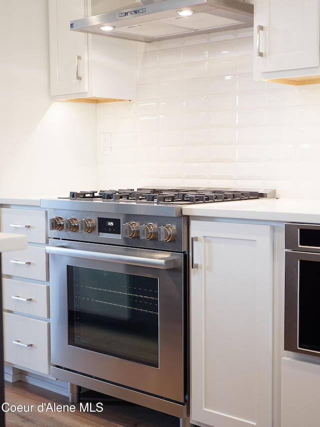 kitchen featuring wood-type flooring, stainless steel range, decorative backsplash, white cabinets, and exhaust hood