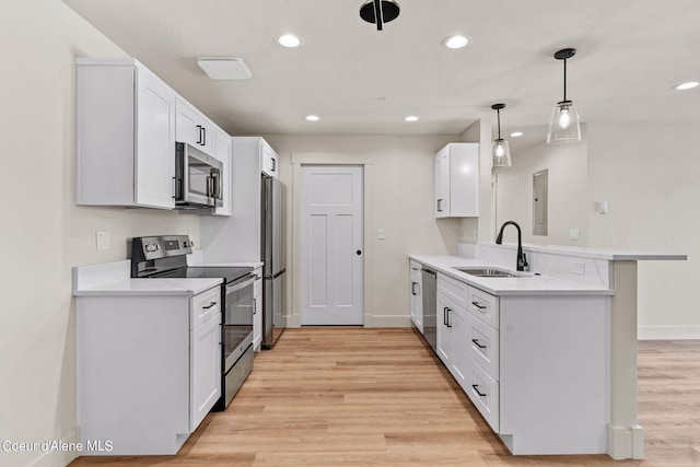 kitchen with a peninsula, light wood-style floors, white cabinets, stainless steel appliances, and a sink