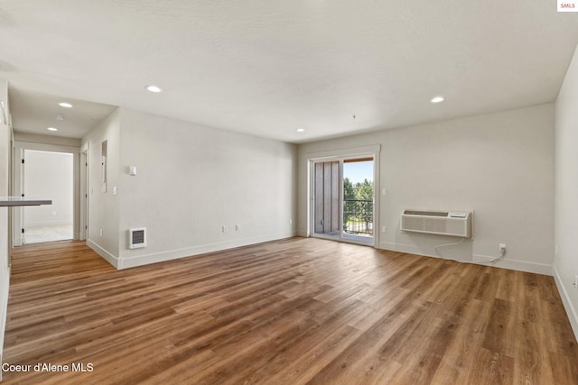 unfurnished living room featuring visible vents, baseboards, an AC wall unit, recessed lighting, and wood finished floors