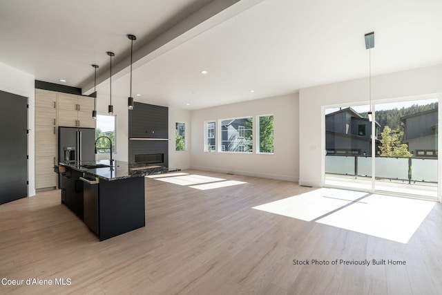 kitchen with light wood-type flooring, sink, an island with sink, hanging light fixtures, and a fireplace