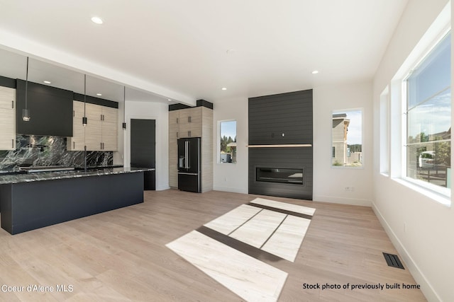 kitchen with light hardwood / wood-style floors, black fridge, a fireplace, backsplash, and dark stone countertops