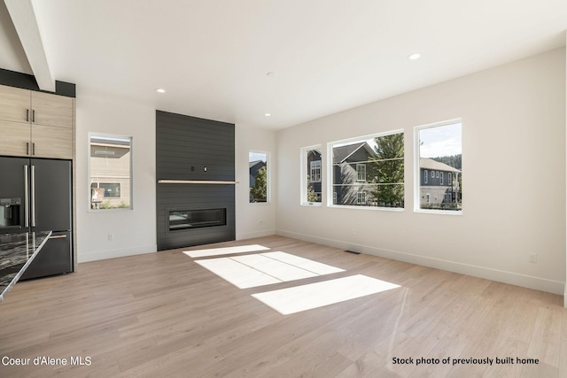 unfurnished living room with a large fireplace, beamed ceiling, and light wood-type flooring