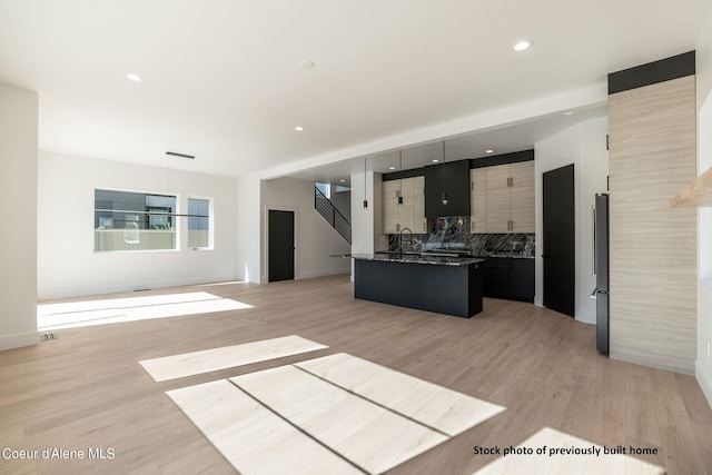 kitchen with stainless steel refrigerator, backsplash, light wood-type flooring, a center island with sink, and sink