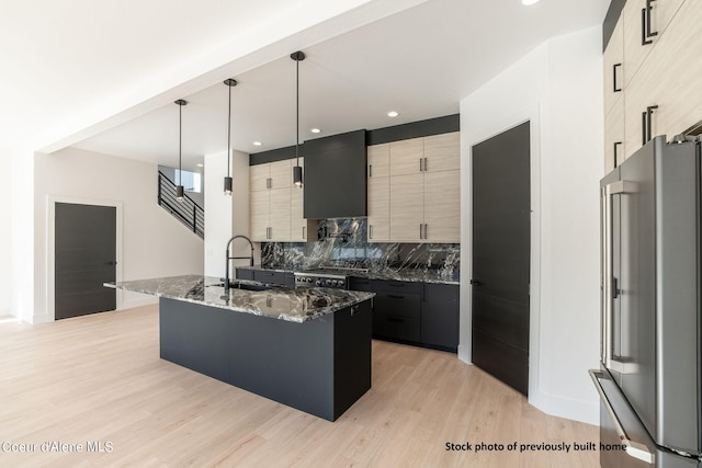 kitchen featuring sink, decorative light fixtures, a center island with sink, stainless steel appliances, and dark stone counters