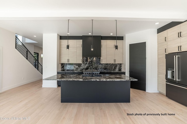 kitchen featuring a center island with sink, dark stone counters, hanging light fixtures, and high end refrigerator