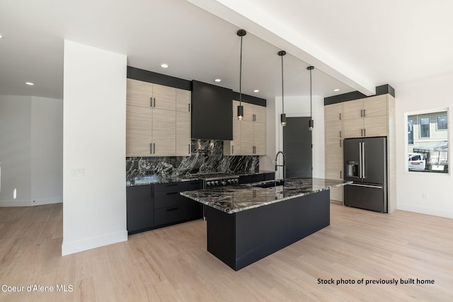 kitchen with sink, high end fridge, a center island with sink, decorative light fixtures, and dark stone counters