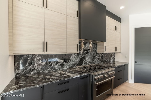 kitchen with light wood-type flooring, dark stone counters, high end range, and light brown cabinets