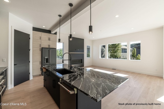 kitchen with pendant lighting, dark stone counters, dishwasher, sink, and a center island with sink