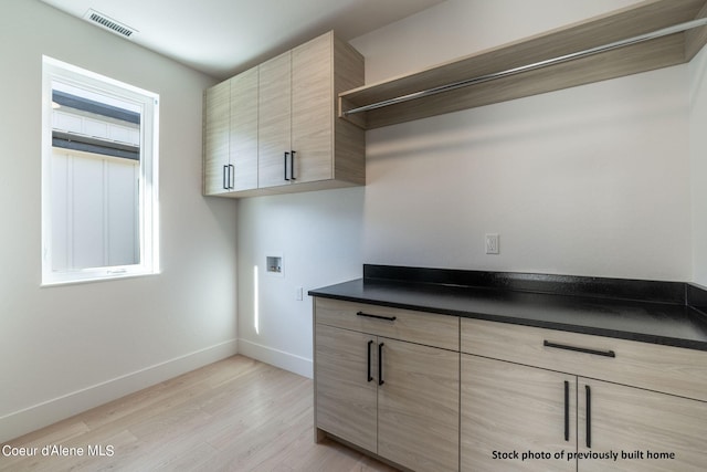 laundry area with hookup for a washing machine, cabinets, and light hardwood / wood-style flooring