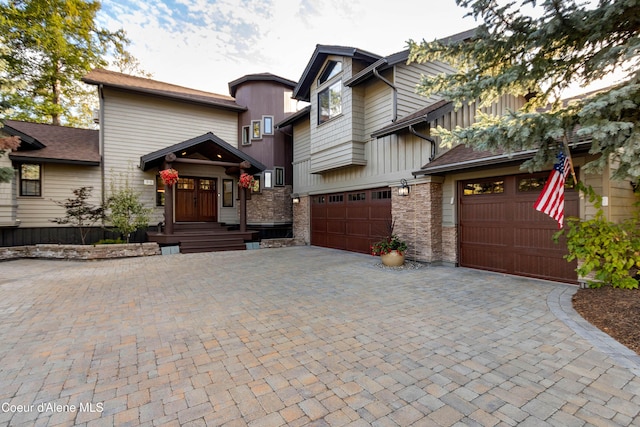 view of front of property with board and batten siding, an attached garage, stone siding, and decorative driveway