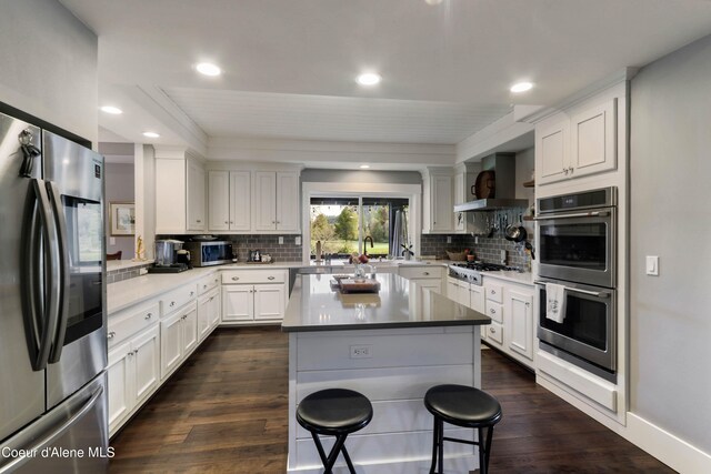 kitchen with a kitchen island, wall chimney range hood, white cabinetry, appliances with stainless steel finishes, and dark hardwood / wood-style flooring