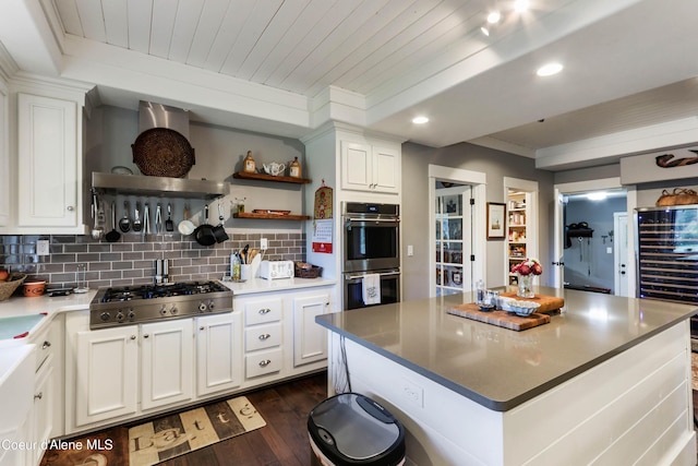 kitchen with tasteful backsplash, white cabinets, exhaust hood, dark wood-style flooring, and appliances with stainless steel finishes