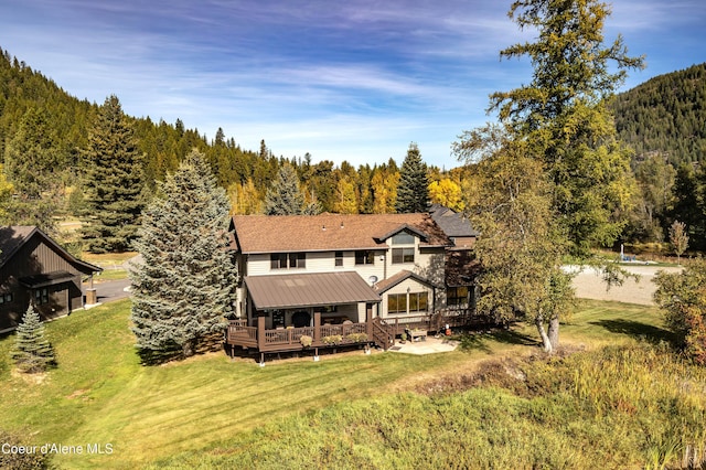 back of house featuring a wooded view, metal roof, a deck, and a lawn
