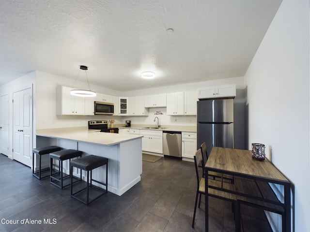 kitchen with dark hardwood / wood-style floors, kitchen peninsula, pendant lighting, white cabinets, and appliances with stainless steel finishes