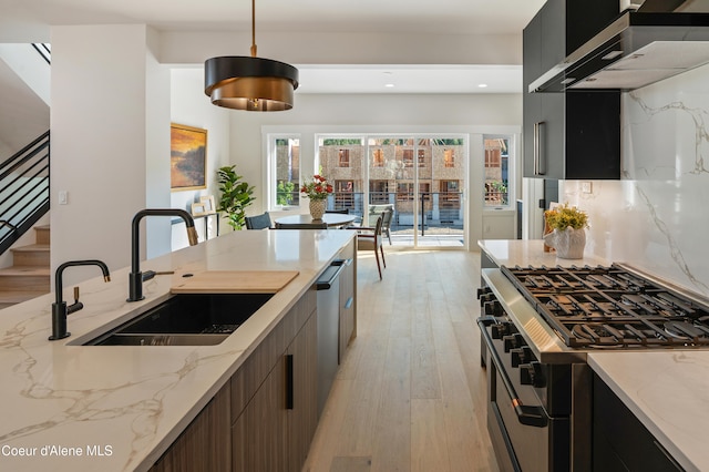 kitchen with pendant lighting, sink, light hardwood / wood-style floors, stainless steel appliances, and wall chimney range hood