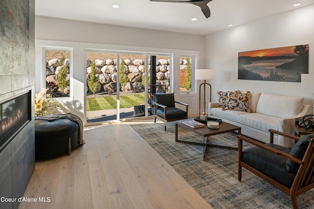 living room featuring ceiling fan, a tiled fireplace, and light hardwood / wood-style floors