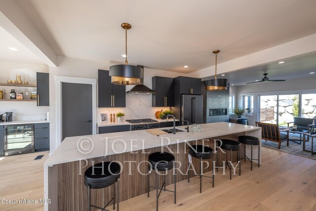 kitchen featuring wall chimney range hood, a breakfast bar area, appliances with stainless steel finishes, hanging light fixtures, and light stone countertops