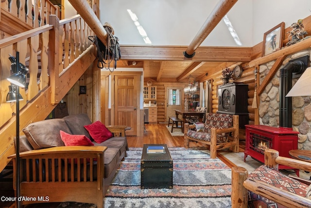 living room featuring beamed ceiling, wood walls, a wood stove, an inviting chandelier, and light hardwood / wood-style floors