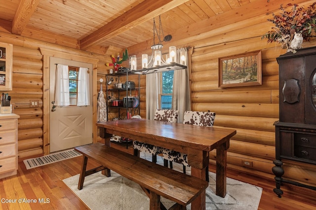 dining area featuring beamed ceiling, a chandelier, rustic walls, and light hardwood / wood-style flooring