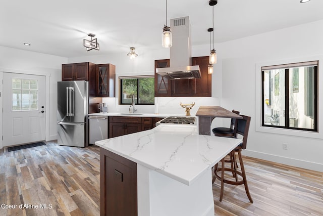 kitchen with light wood-type flooring, island exhaust hood, a peninsula, stainless steel appliances, and a sink
